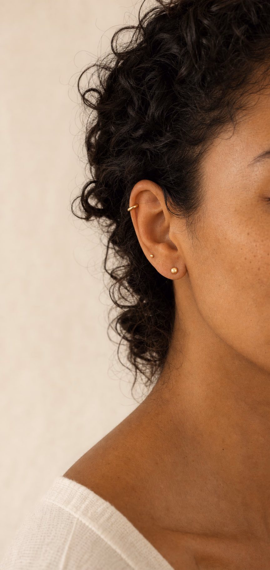 Mulher adulta de pele morena com uma composição auricular delicada em joias douradas